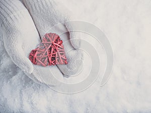 Female hands in white knitted mittens with a entwined vintage romantic red heart on a snow. Love and St. Valentine concept.