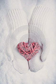 Female hands in white knitted mittens with a entwined vintage romantic red heart on a snow. Love and St. Valentine concept.