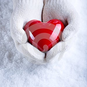 Una donna mani bianco lavorato maglia guanti brillante cuore rosso sul la neve. un San Valentino accogliente 