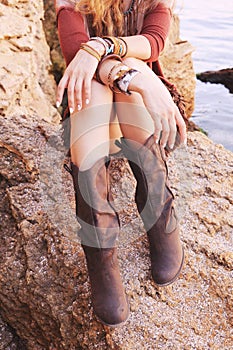 Female hands with white manicure and boho chic bracelets and legs dressed in leather boots photo