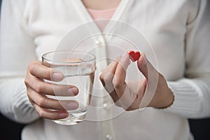 Female hands with white shirt is holding red pill in heart shape