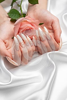 Female Hands on a white silk background with beautiful pearl manicure.
