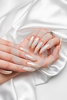 Female Hands on a white silk background with beautiful pearl manicure.Hands on a brown background and beautiful pearl manicure