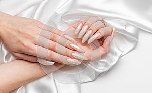 Female Hands on a white silk background with beautiful pearl manicure.Hands on a brown background and beautiful pearl manicure