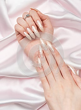 Female Hands on a white silk background with beautiful pearl manicure.Hands on a brown background and beautiful pearl manicure