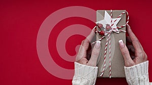 Female hands white sweater hold Christmas New Year gift box on red background,top view,flat lay,copy space. Christmas holidays