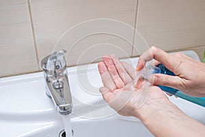 Female hands, woman washing and desinfecting hands in a bathroom, squeezing antybacterial liquid soap from a plastic bottle to a