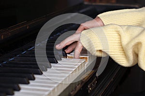 Female hands in wool sweater sleeves playing on piano
