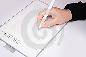 Female hands work on a graphic tablet. Hand holds stylus pen and draws. White graphic tablet. The work of a graphic designer. Girl