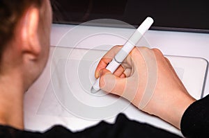 Female hands work on a graphic tablet. Hand holds stylus pen and draws. White graphic tablet. The work of a graphic designer. Girl