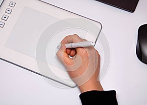 Female hands work on a graphic tablet. Hand holds stylus pen and draws. White graphic tablet. The work of a graphic designer. Girl