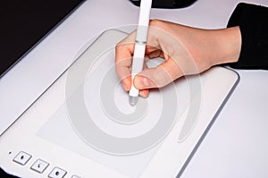 Female hands work on a graphic tablet. Hand holds stylus pen and draws. White graphic tablet. The work of a graphic designer. Girl