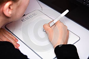 Female hands work on a graphic tablet. Hand holds stylus pen and draws. White graphic tablet. The work of a graphic designer. Girl