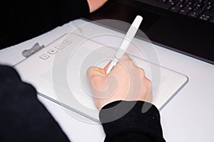 Female hands work on a graphic tablet. Hand holds stylus pen and draws. White graphic tablet. The work of a graphic designer. Girl