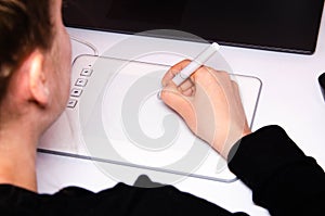 Female hands work on a graphic tablet. Hand holds stylus pen and draws. White graphic tablet. The work of a graphic designer. Girl