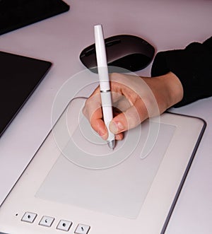 Female hands work on a graphic tablet. Hand holds stylus pen and draws. White graphic tablet. The work of a graphic designer. Girl