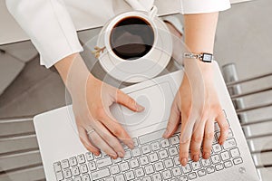 Female hands work on a modern laptop. Next to a cup of coffee