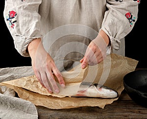 female hands are wrapped in brown paper whole fresh sea bass fish