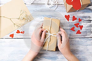 Female hands wrapping a gift in craft paper on a white wooden background, present packaging at home