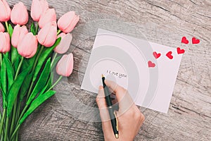 Female hands write a message of love on a white envelope, on a wooden background. Valentine`s Day