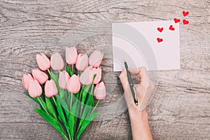 Female hands write a message of love on a white envelope, on a wooden background. Valentine`s Day