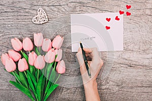 Female hands write a message of love on a white envelope, on a wooden background. Valentine`s Day