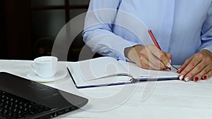 Female hands write to do list on blank notepad, drink coffee. Close up business lady hand writing company profit in her notebook.