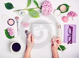 Female hands write To do list on the white working place with female accessories, cup of coffee, notebook, glasses, and wisteria f photo