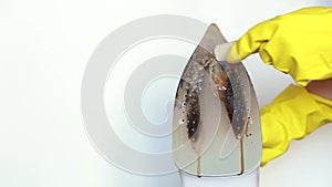 Female hands in yellow gloves clean the dirty surface of the iron with a special pencil.