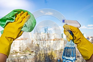 Female hands in yellow gloves cleaning window with green rag and spray detergent. Spring cleanup, housework concept