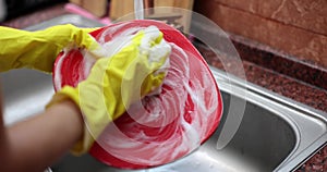 Female hands in yellow protective rubber gloves washing red plate