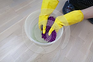 Female hands in yellow rubber gloves wringing water out of purple rag