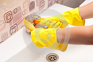 Female hands with yellow rubber protective gloves cleaning tap with orange cloth