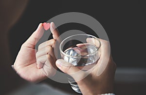 Female handsis holding red pill in heart shape and glass of water