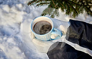 female handswith a blue mug of steaming coffee on the background of a winter forest photo