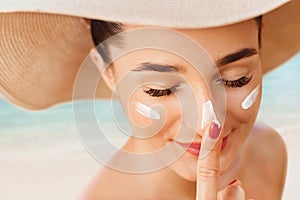 Female in hat applying  moisturizing lotion on skin. Beautiful Young woman with sun cream on face.Skin care. Sun protection.