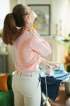 Female having neck pain while ironing on ironing board