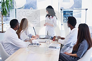 Female head doctor reading a lecture on the meeting at modern clinic. Professional doctors of multi ethnic group examine