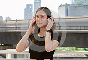 Female with headphones standing outdoors in the city. Fitness woman relaxing and listening music during her workout