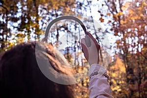 Female with headphones walking on the park listen sounds or music of autumn forest. Concept. Indian summer season