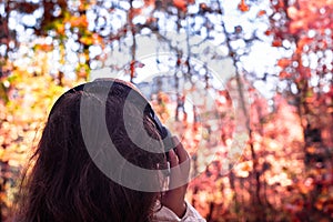 Female with headphones walking on the park listen sounds or music of autumn forest. Concept. Indian summer season