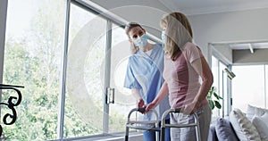 Female health worker assisting senior woman to walk with walking frame at home