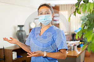 Female health worker in blue uniform and mask welcoming to clinic