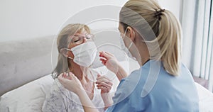 Female health worker putting face mask on senior woman at home
