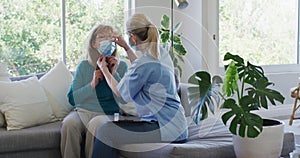 Female health worker putting face mask on senior woman at home