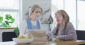 Female health worker and senior woman discussing over laptop at home