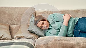Female health. Young sad woman lying on the couch at home and suffering from menstrual period or abdominal pain