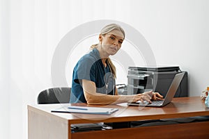 Female healthcare worker doing some paperwork and using laptop while working at doctor& x27;s office
