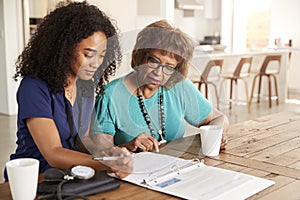 Female healthcare worker filling in a form with a senior woman during a home health visit