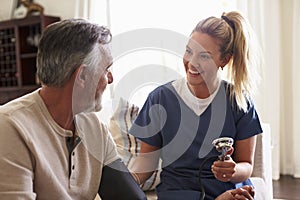 Female healthcare worker making home visit to a senior man, taking his blood pressure, close up